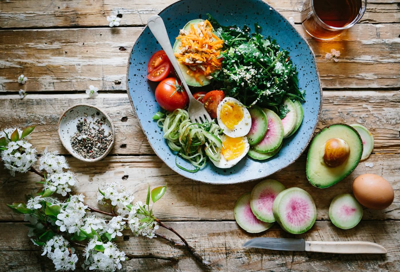 An overhead view of a bowl of fresh vegetables, avocado and egg