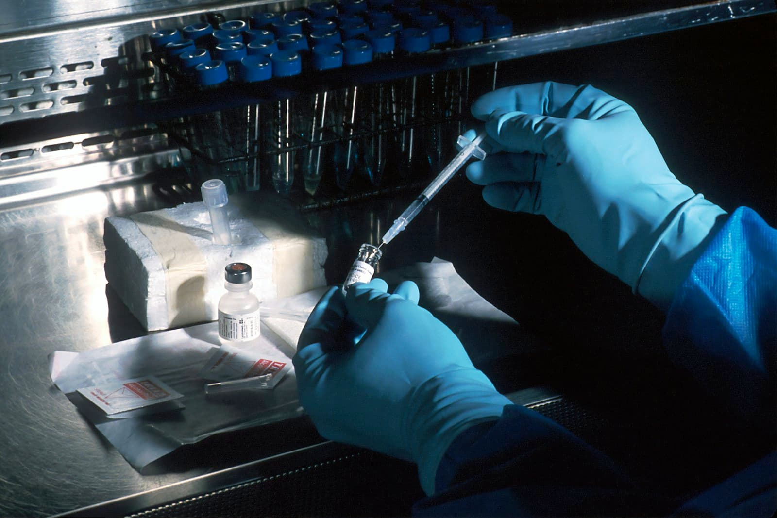 Gloved hands drawing medication from a vial in a laboratory setting