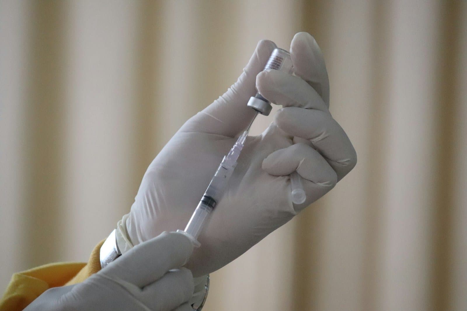 Gloved hands drawing medication from a glass vial into a syringe